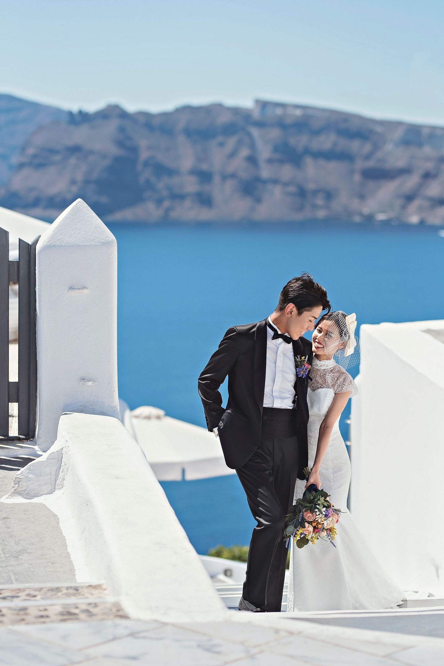 Elegant wedding couple posing against white architecture and blue sea in Santorini.