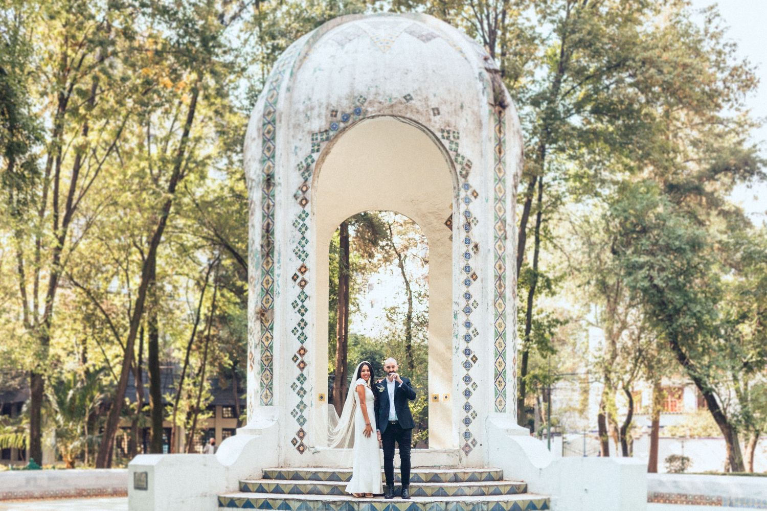Wedding couple posing under decorative white arches in outdoor garden setting.