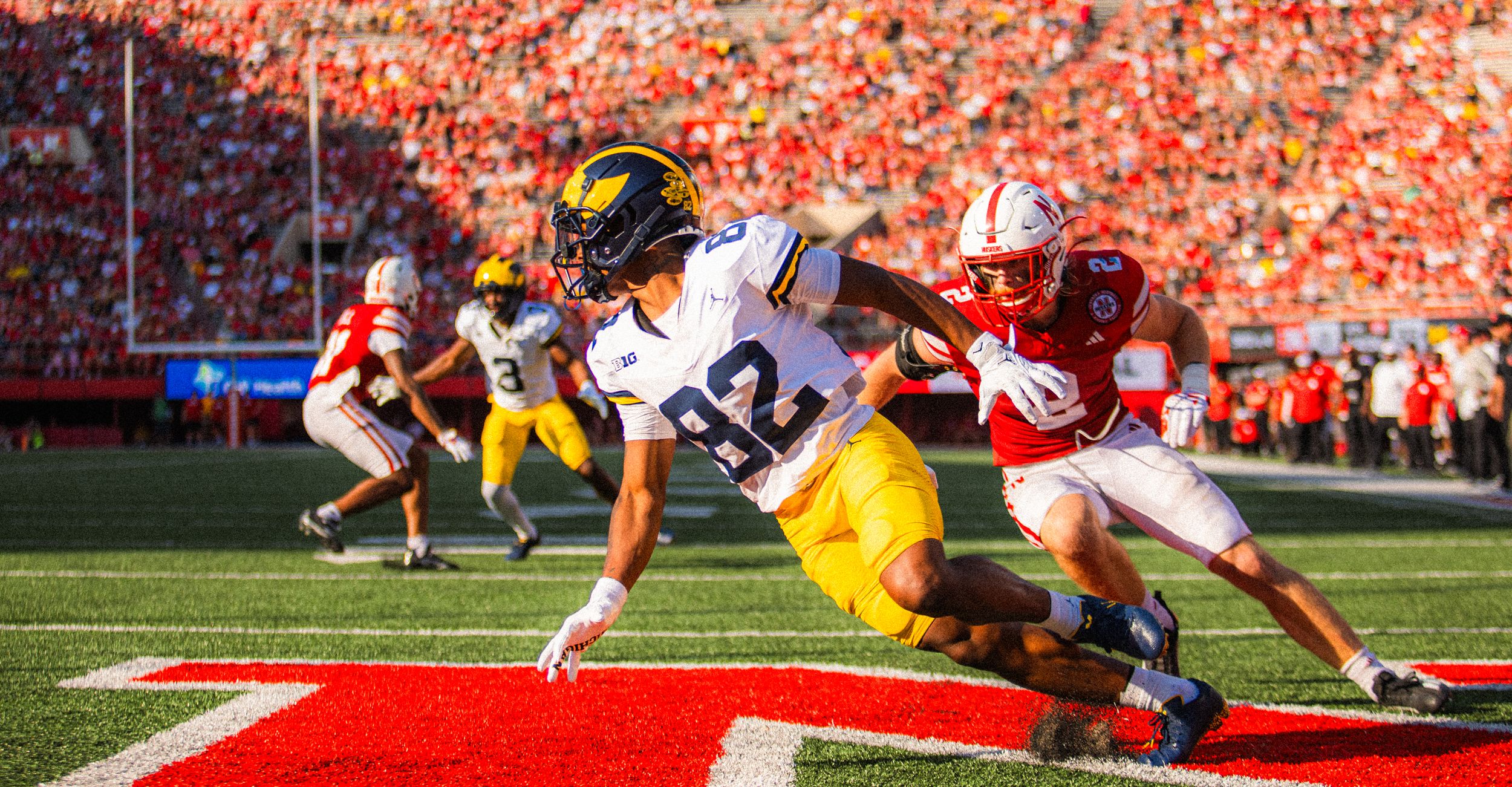 Football player in yellow uniform diving for extra yards against red-uniformed defenders.