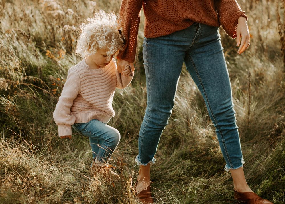 Parent and child walking through autumn field in matching earthy tones.
