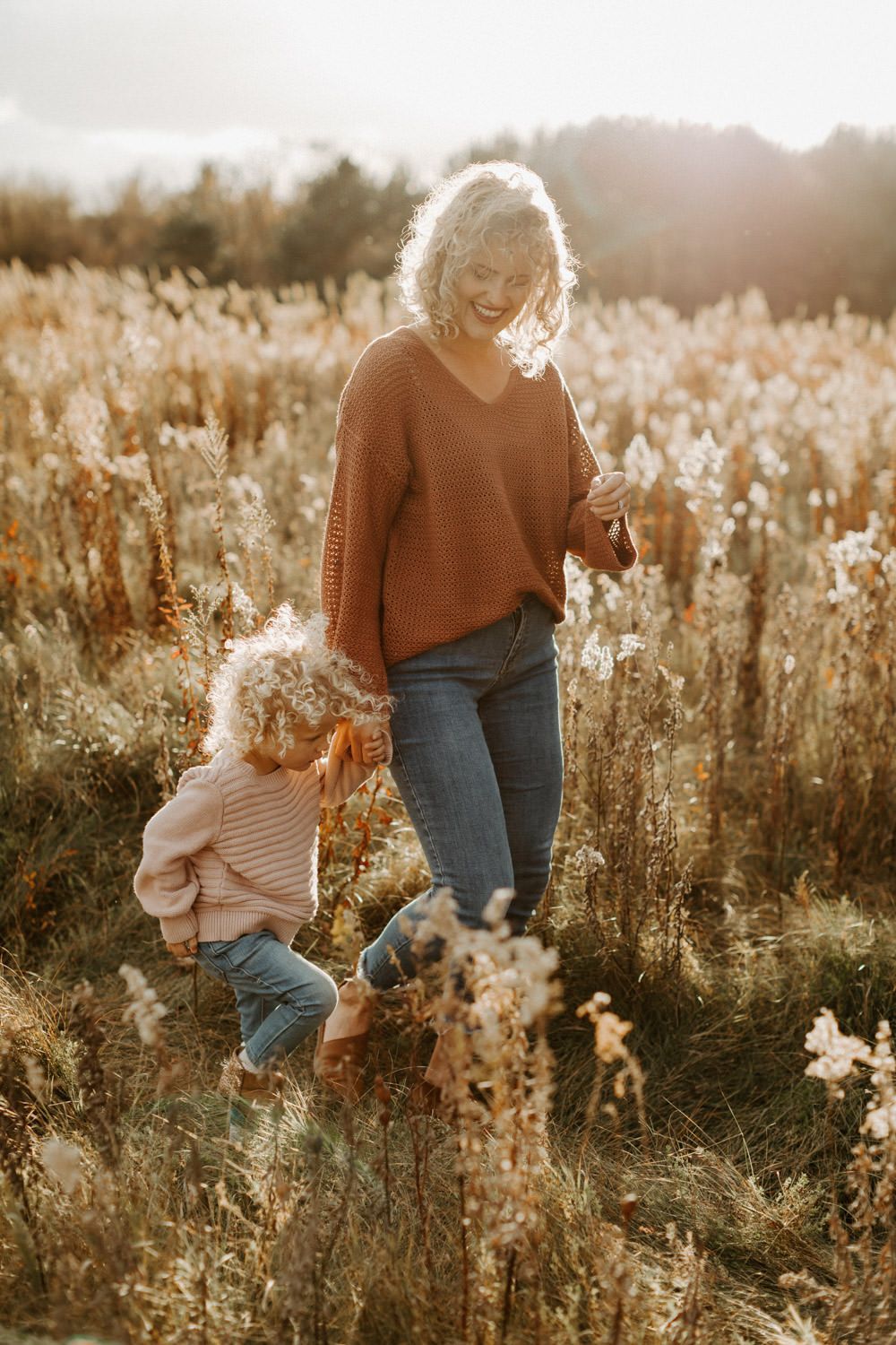 Mother and child walking through sunlit field of golden grass.
