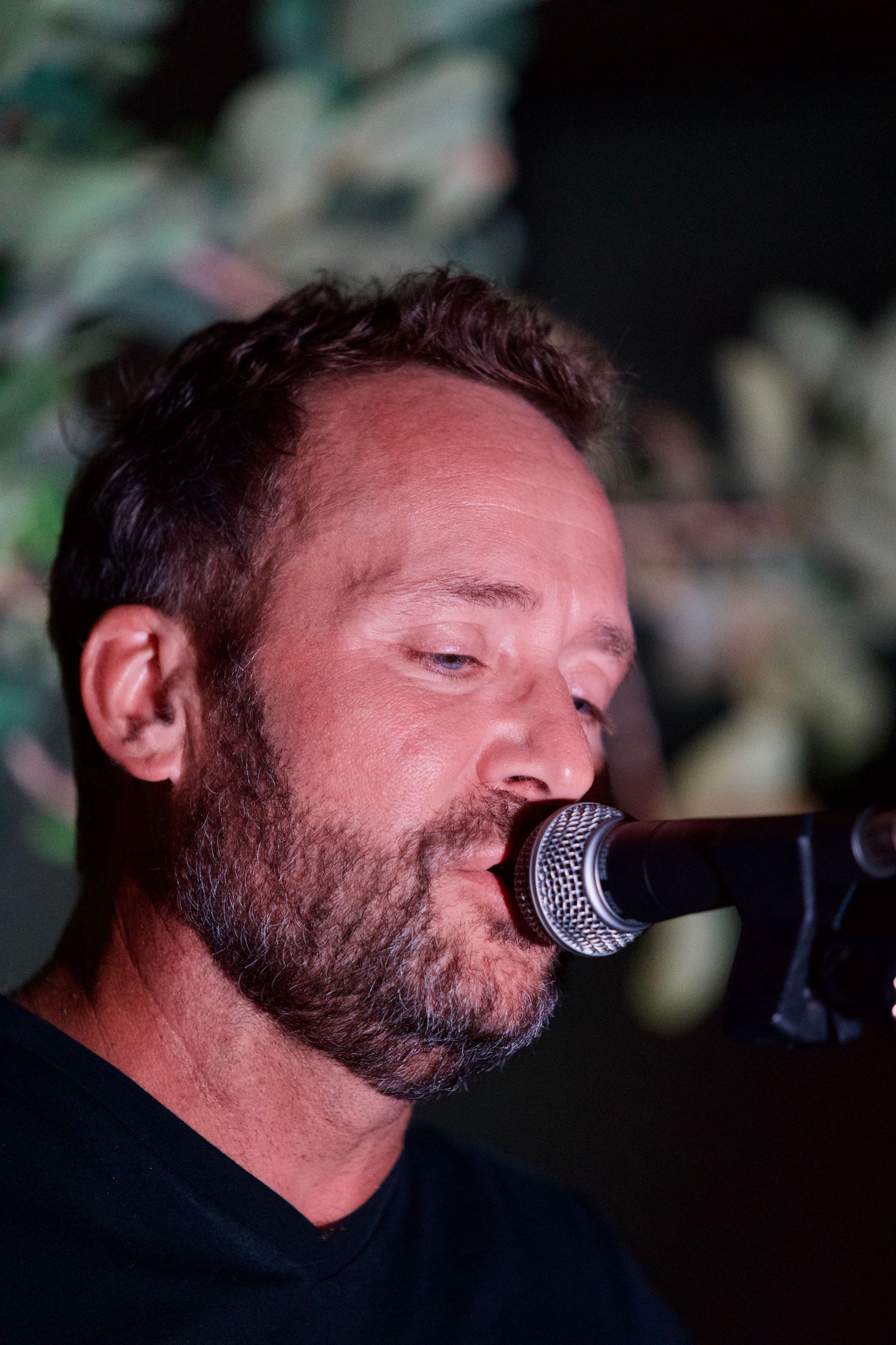Musician singing into microphone in dark lighting conditions.