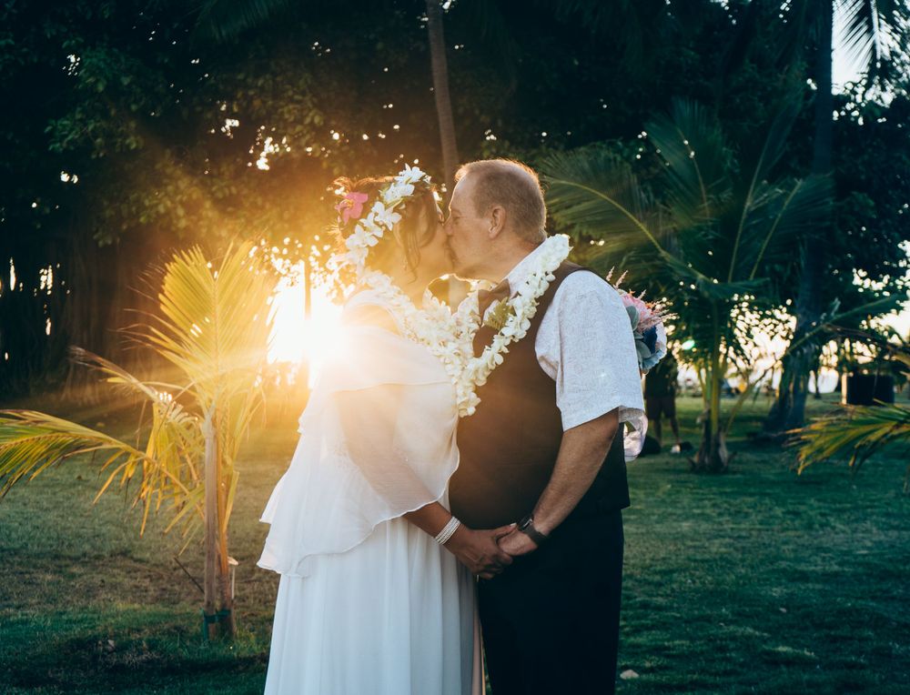 A wedding portrait backlit by golden sunlight through tropical palm trees.