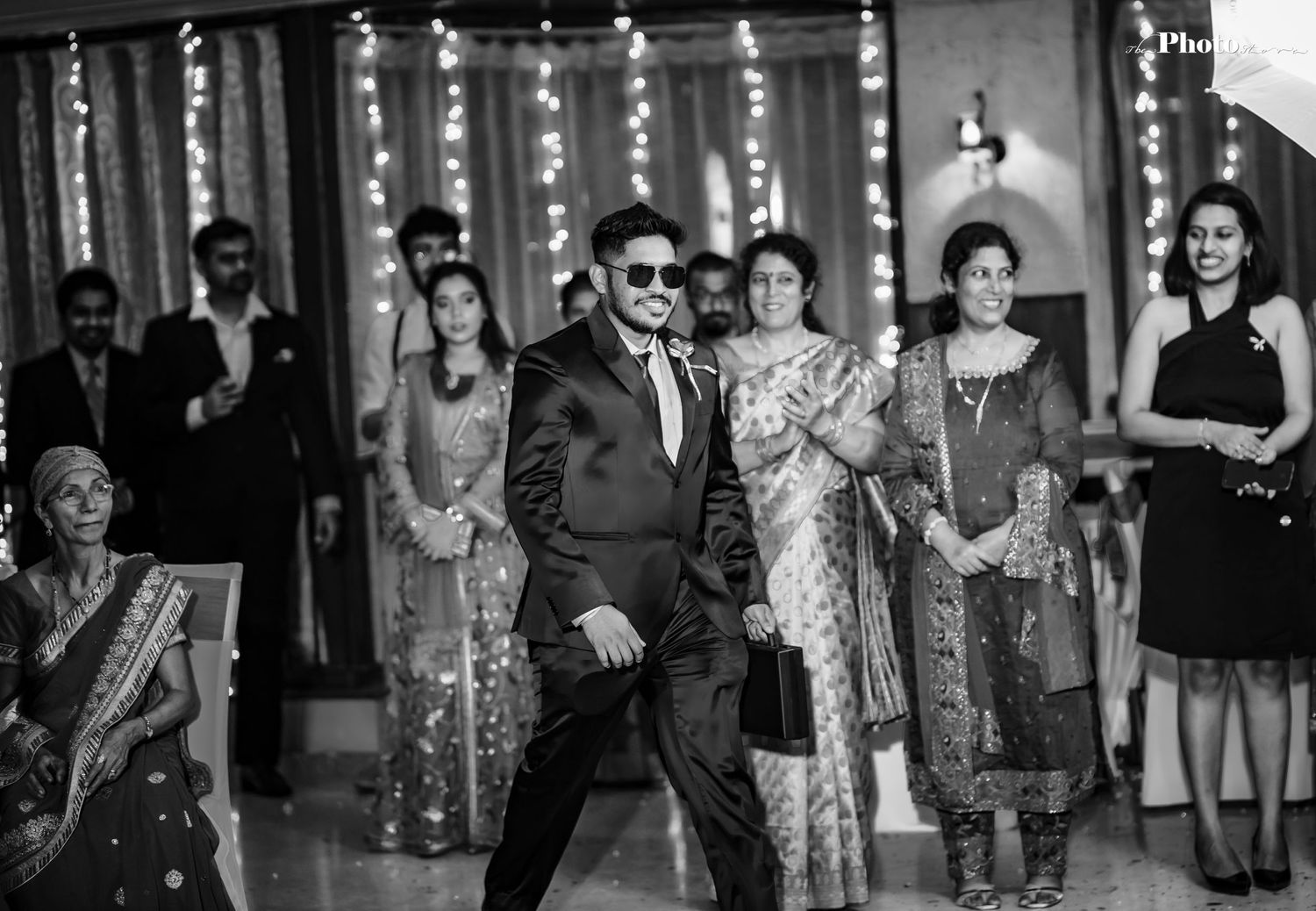 A black and white photo of wedding guests dancing and celebrating at a reception.