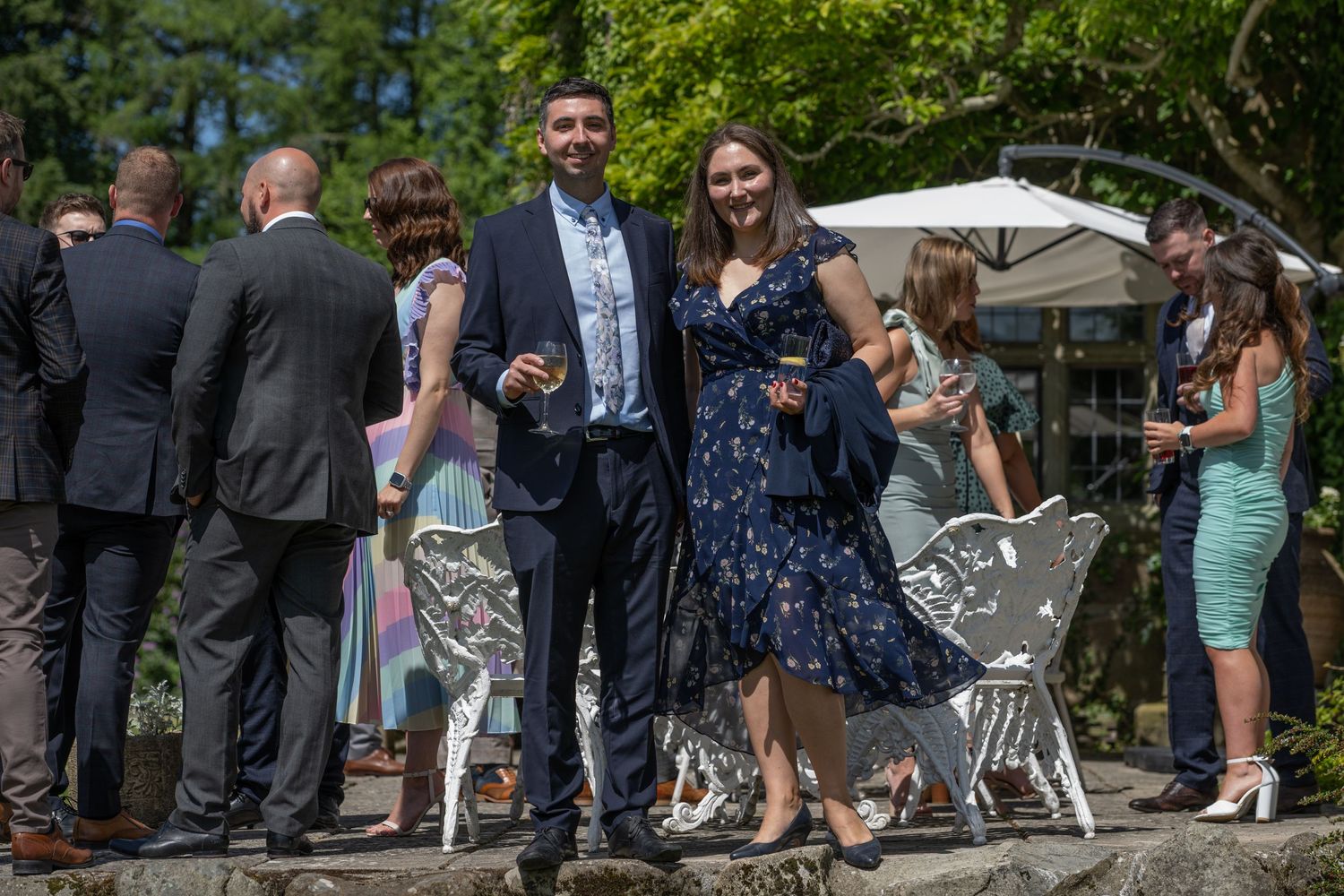 Wedding guests mingling at an outdoor reception with garden furniture.