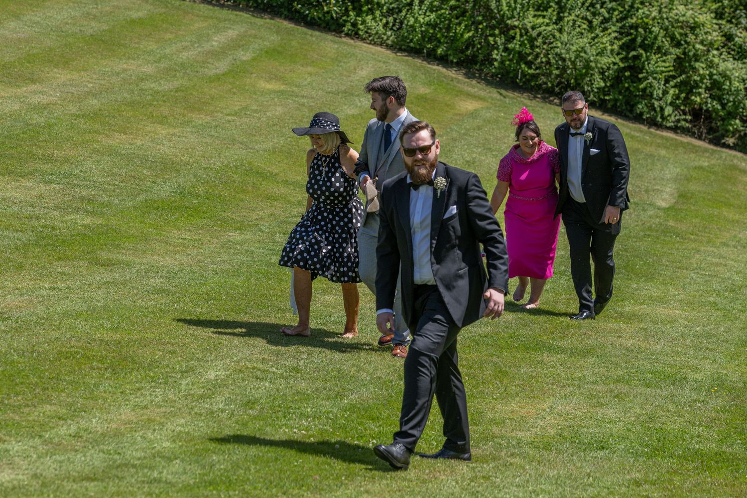 Wedding guests walking across a manicured lawn during an outdoor celebration.
