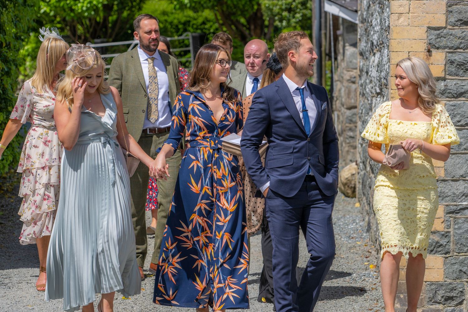 Elegantly dressed wedding guests walking together on a stone path outdoors.