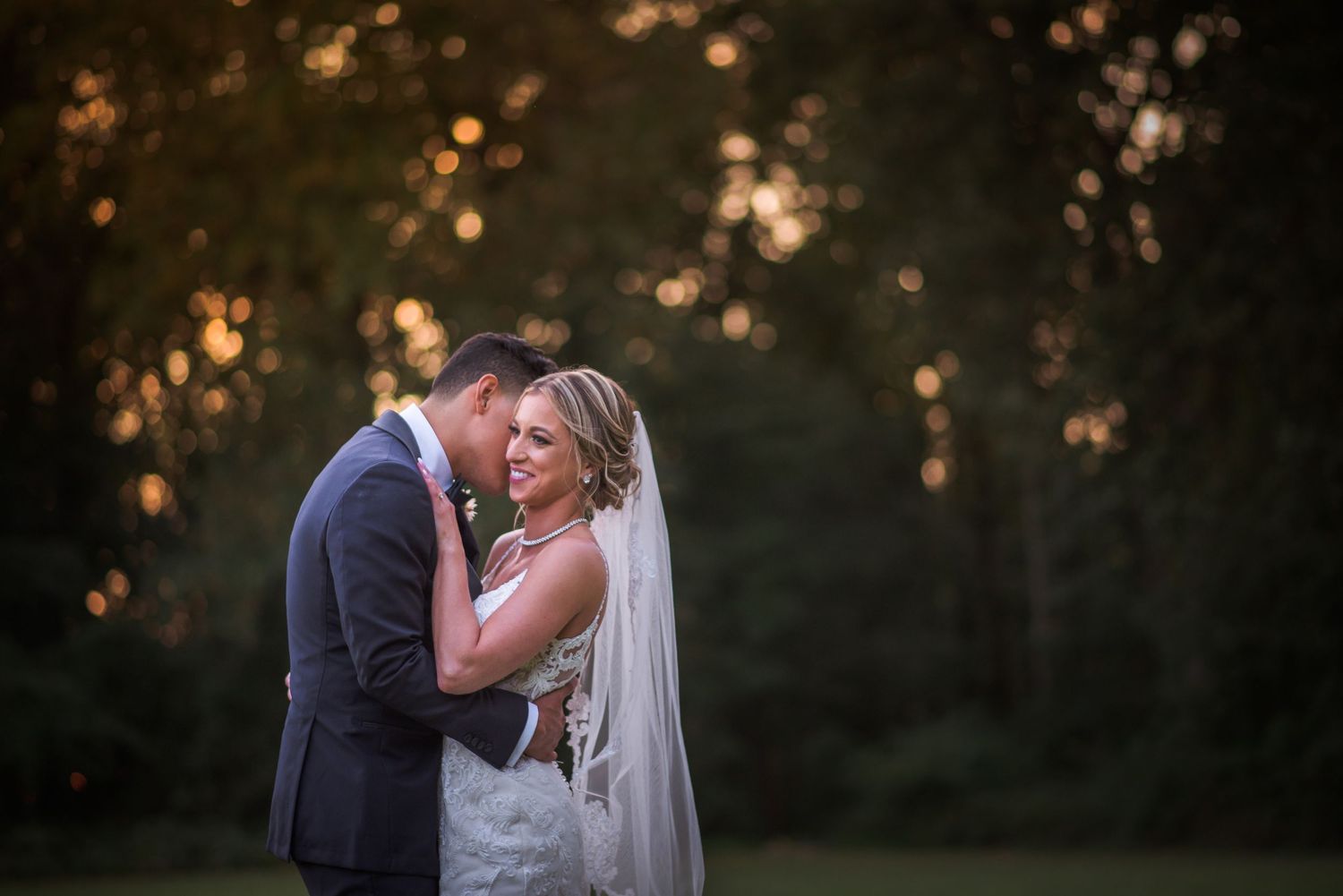 Bride and groom embrace tenderly in warm golden bokeh light at sunset.