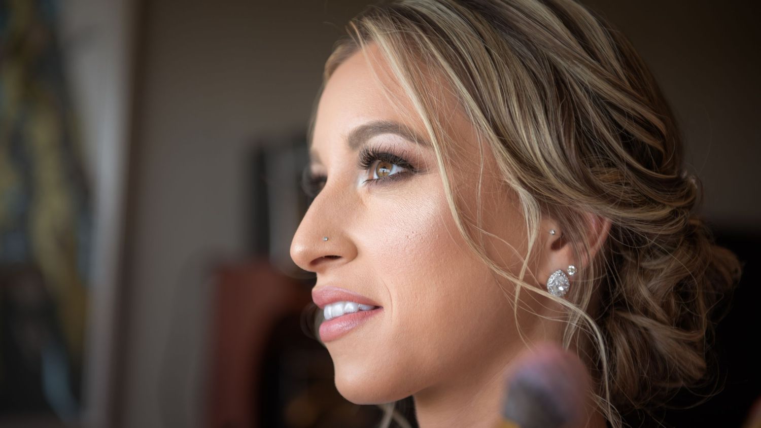 Close-up profile of a bride with elegant updo hairstyle and sparkling earrings on her wedding day.