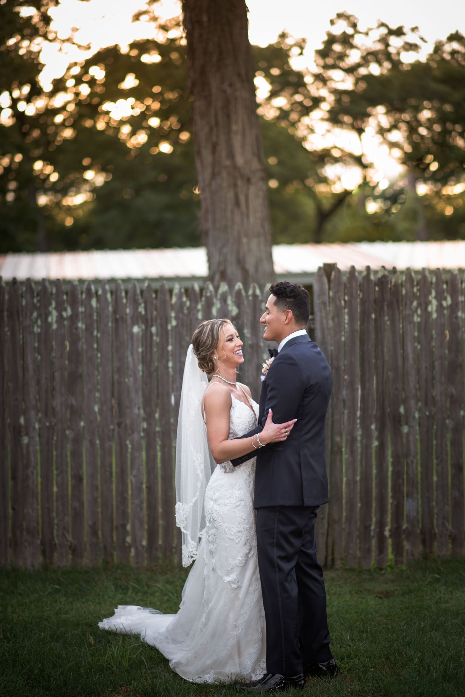 Bride and groom share romantic moment in golden hour light by wooden fence.