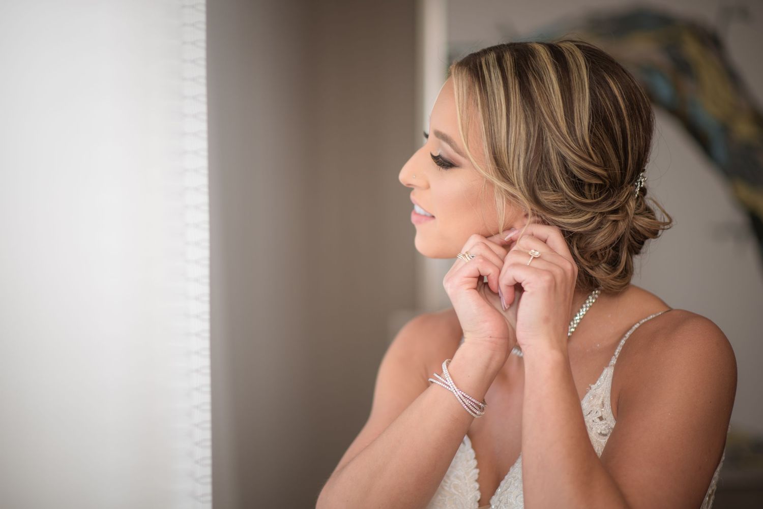 Bride with an elegant updo puts on pearl earrings while getting ready for her wedding ceremony.