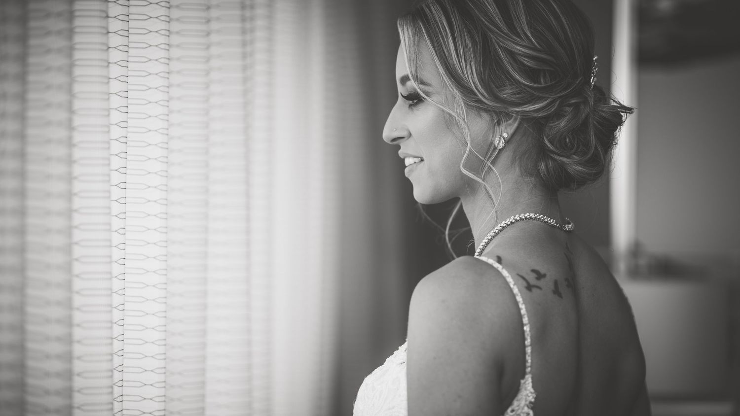 Black and white profile portrait of a bride in a wedding gown standing by a window.