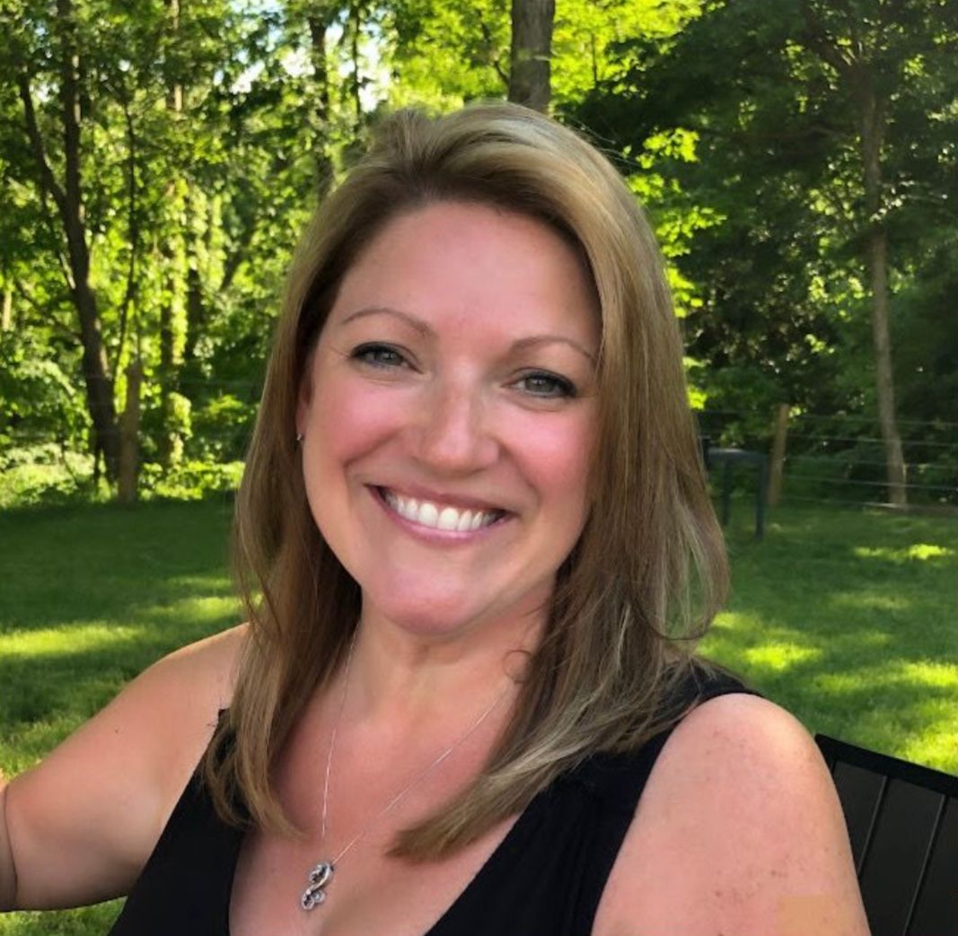 Summer outdoor portrait of a woman smiling in a black top with trees in background.