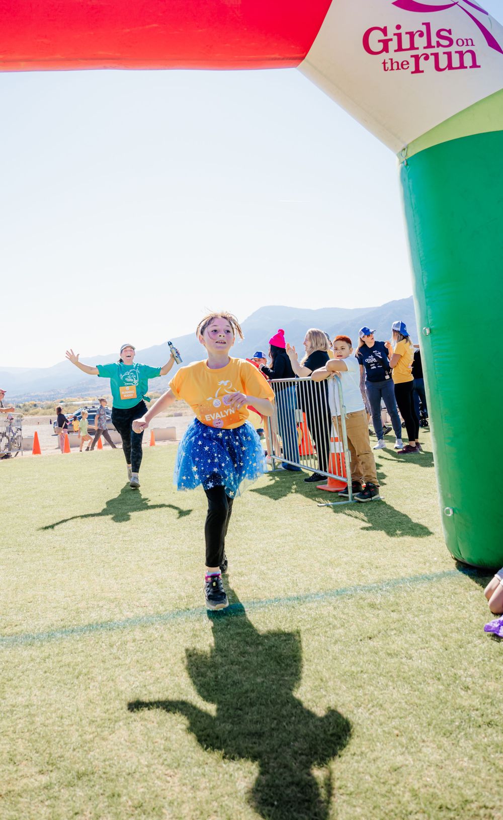 Runner in yellow shirt and blue tutu crosses finish line at Girls on the Run event.