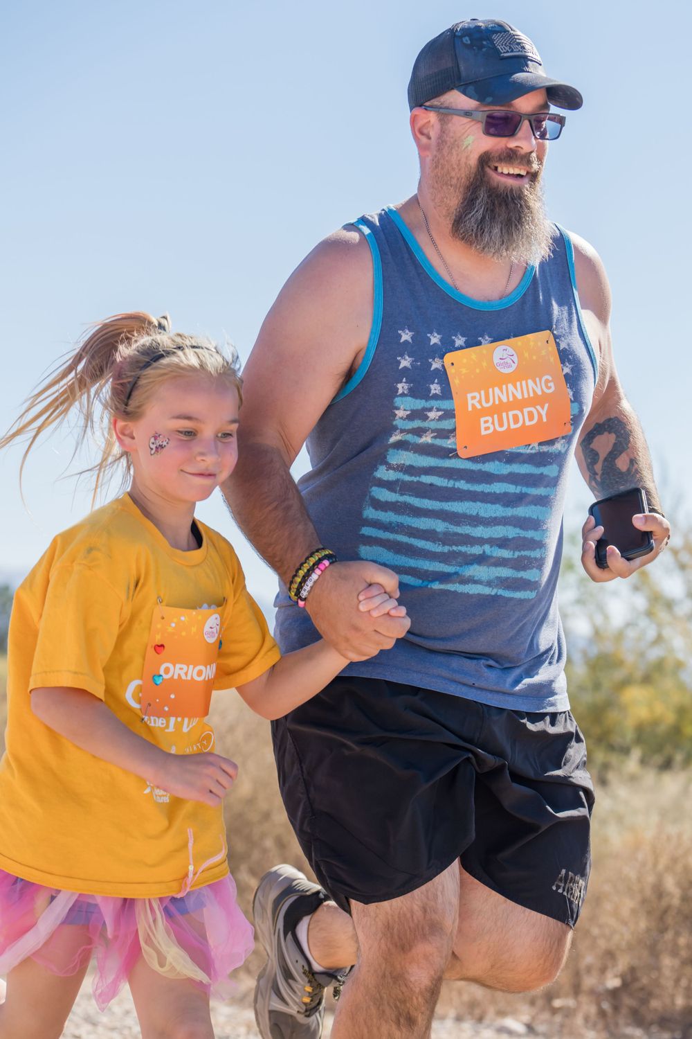 Running buddies in matching orange badges jog together during an outdoor event.