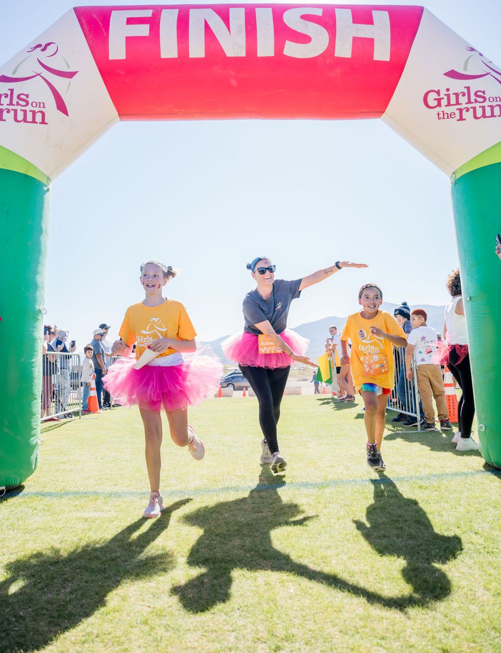 Three runners cross finish line under colorful arch at Girls on the Run event.