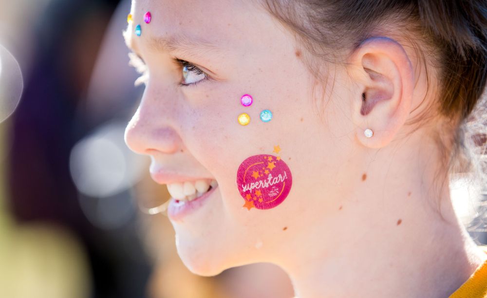 Close-up profile of participant with colorful face stickers at outdoor event.