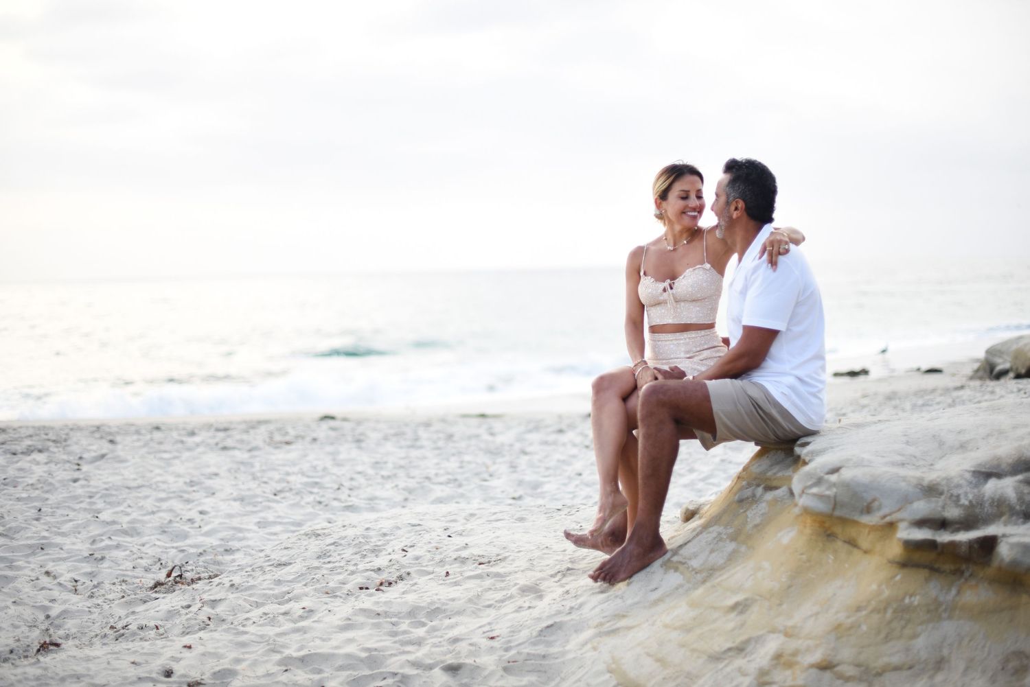 Couple relaxing on rocky beach overlook during sunset.