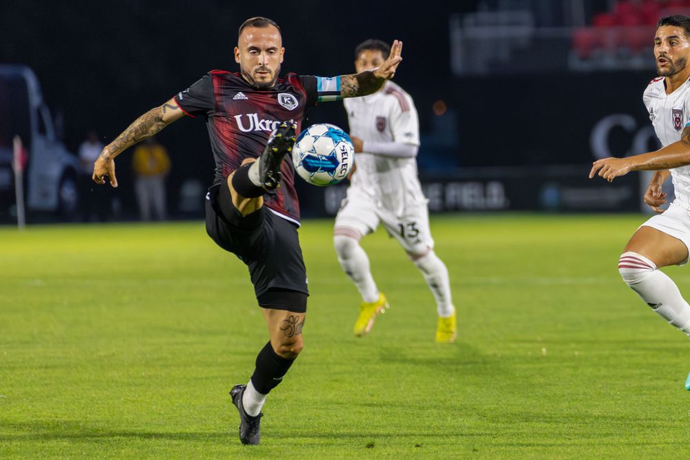 Soccer player in dark uniform attempts to control airborne ball during match.