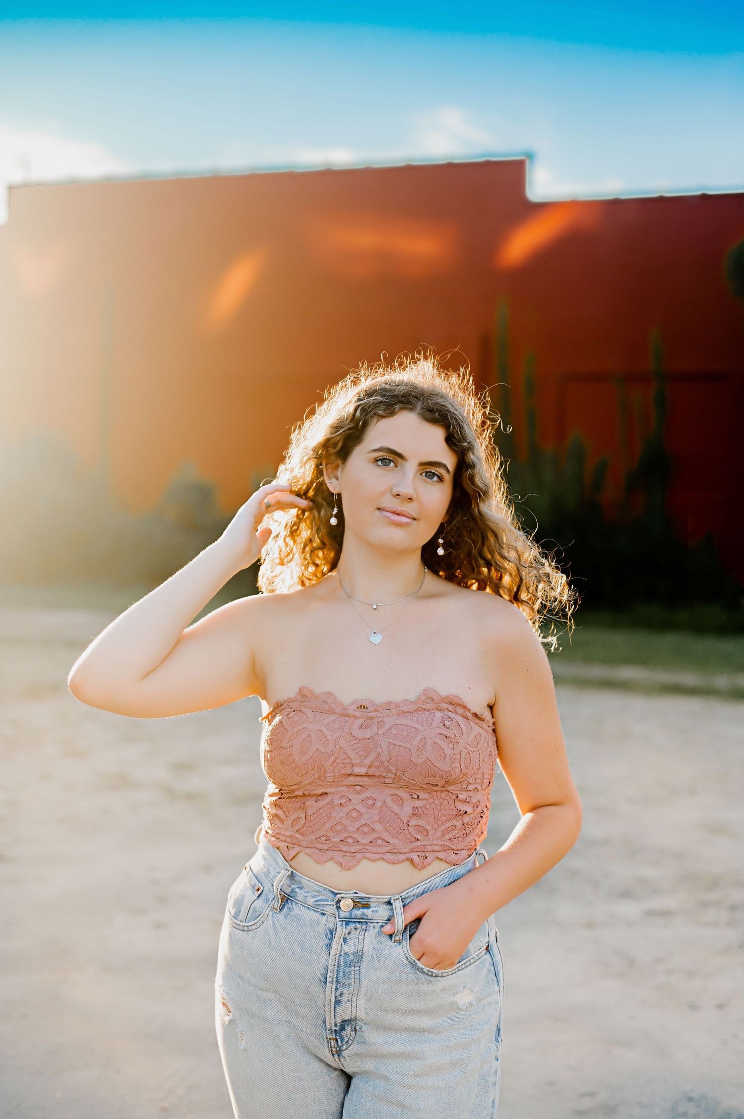 A sunset portrait against an orange wall featuring casual denim and a lace top.