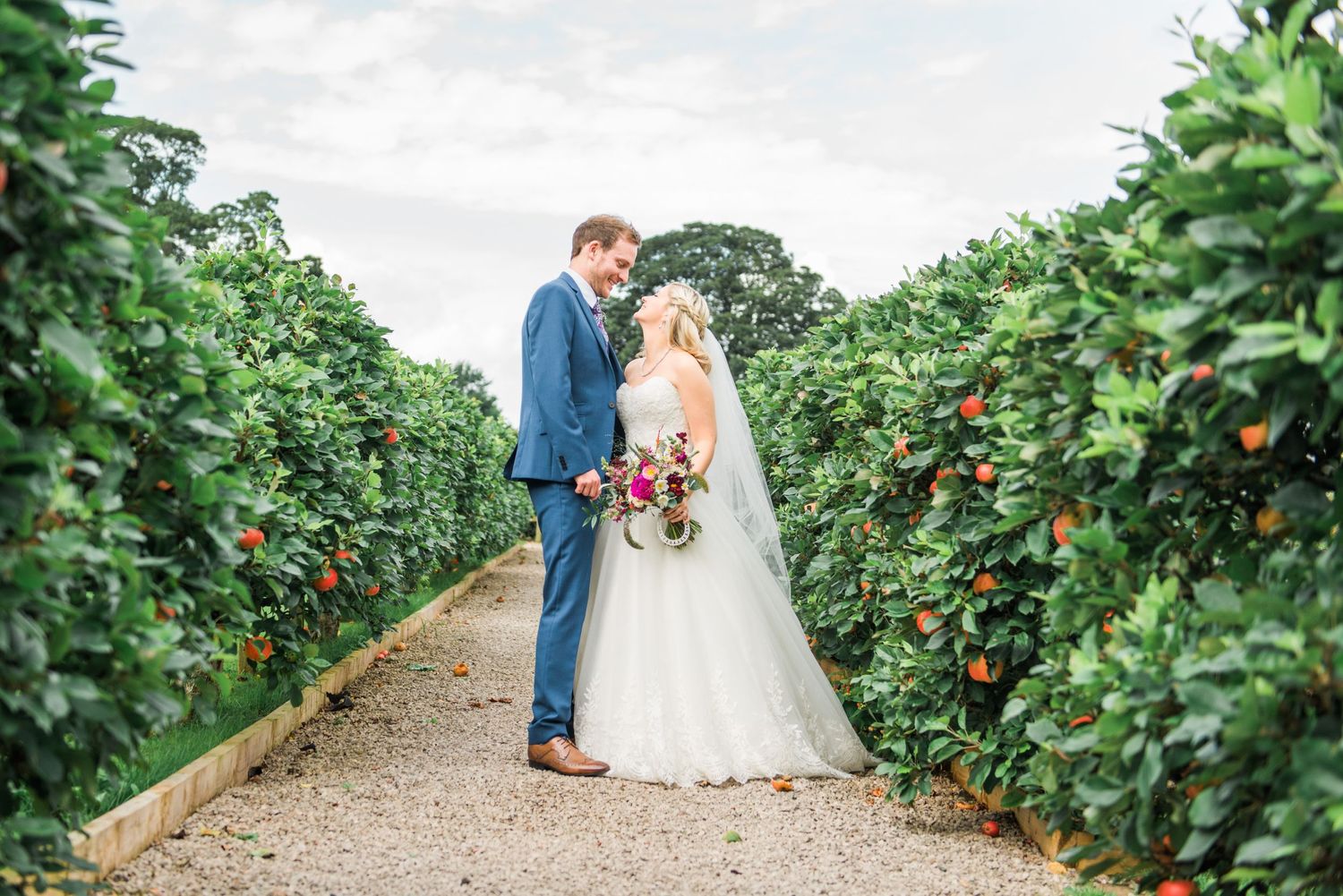bride and groom pausing as they walk through an orchard after their Askham Hall Wedding