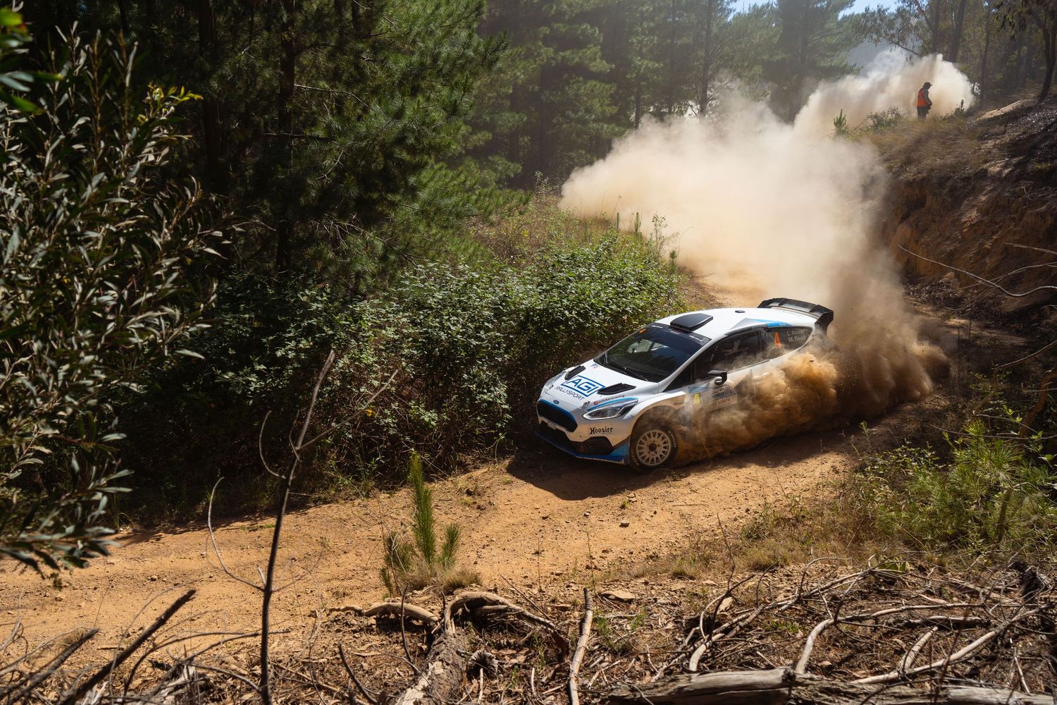 Rally car kicking up dust while navigating steep dirt hill climb.