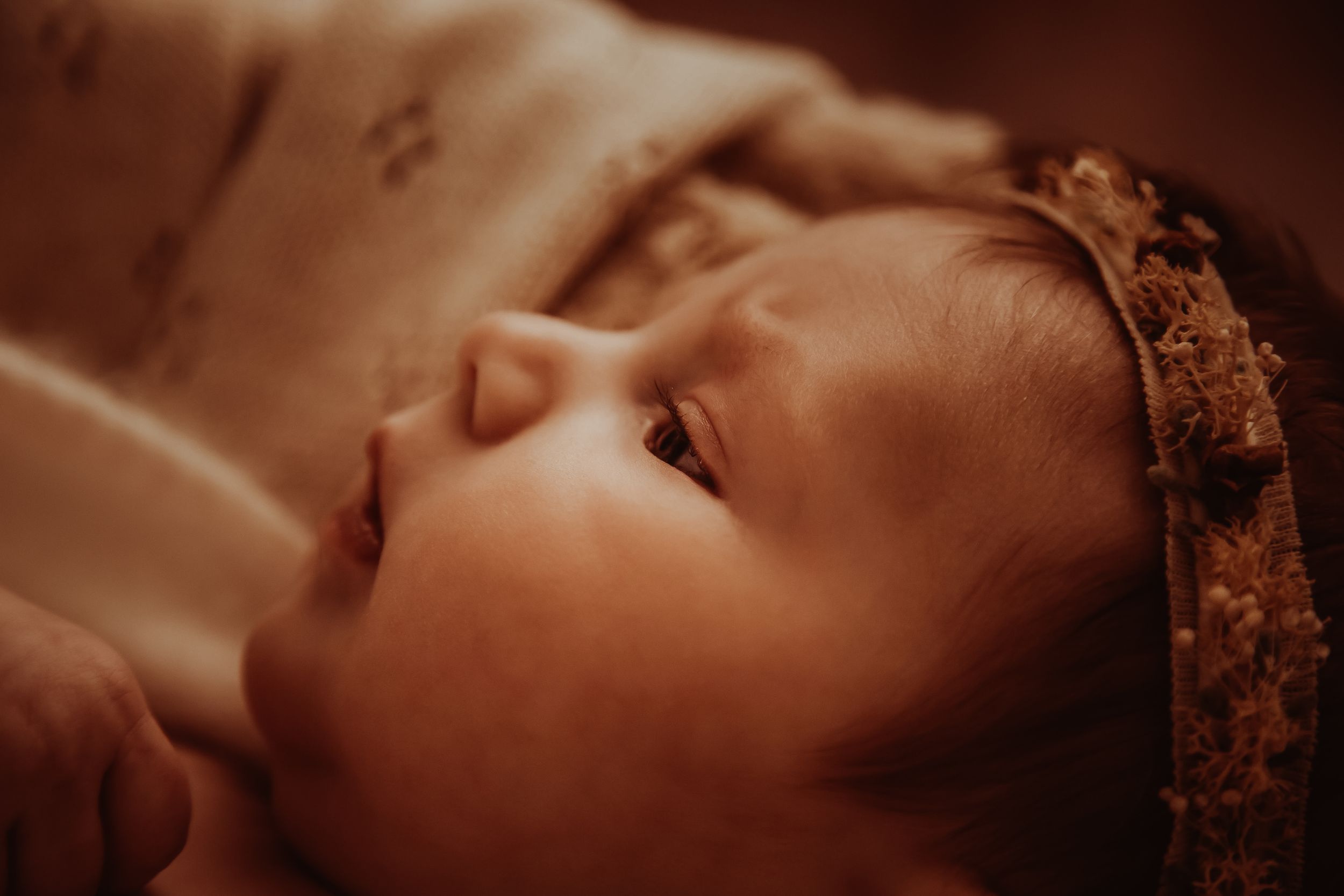 A sleeping baby with a lace headband captured in warm sepia tones.