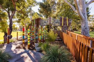 Colorful outdoor playground with wooden walkway and painted poles among eucalyptus trees.