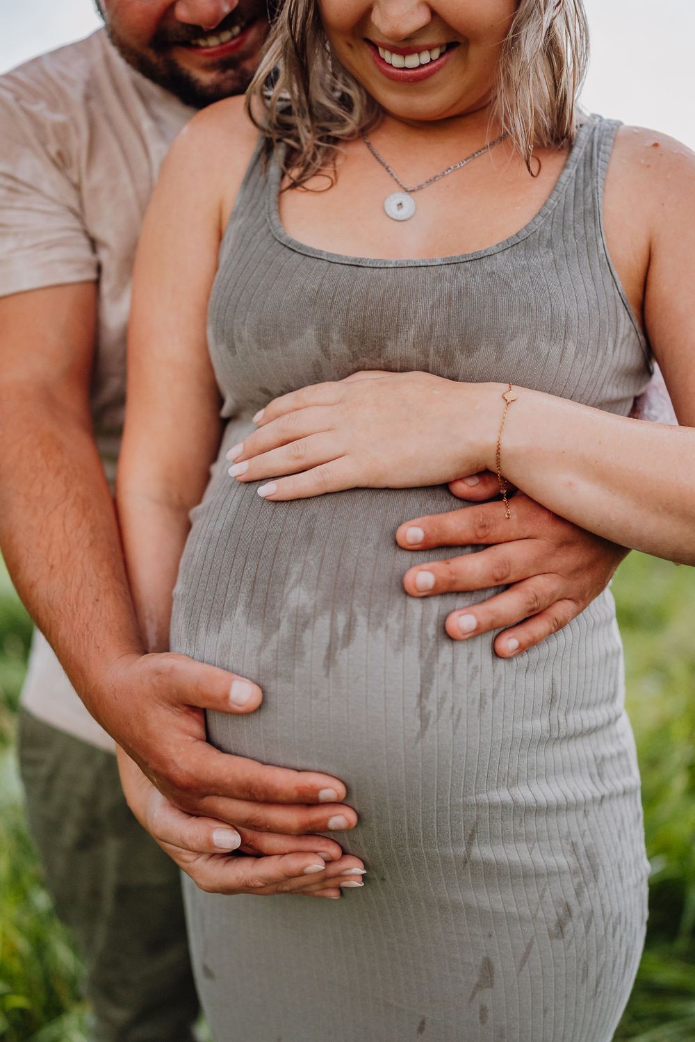 Nahaufnahme von Schwangerschaftsfoto, die Hände zeigen, die einen schwangeren Bauch in einem grauen Kleid wiegen.