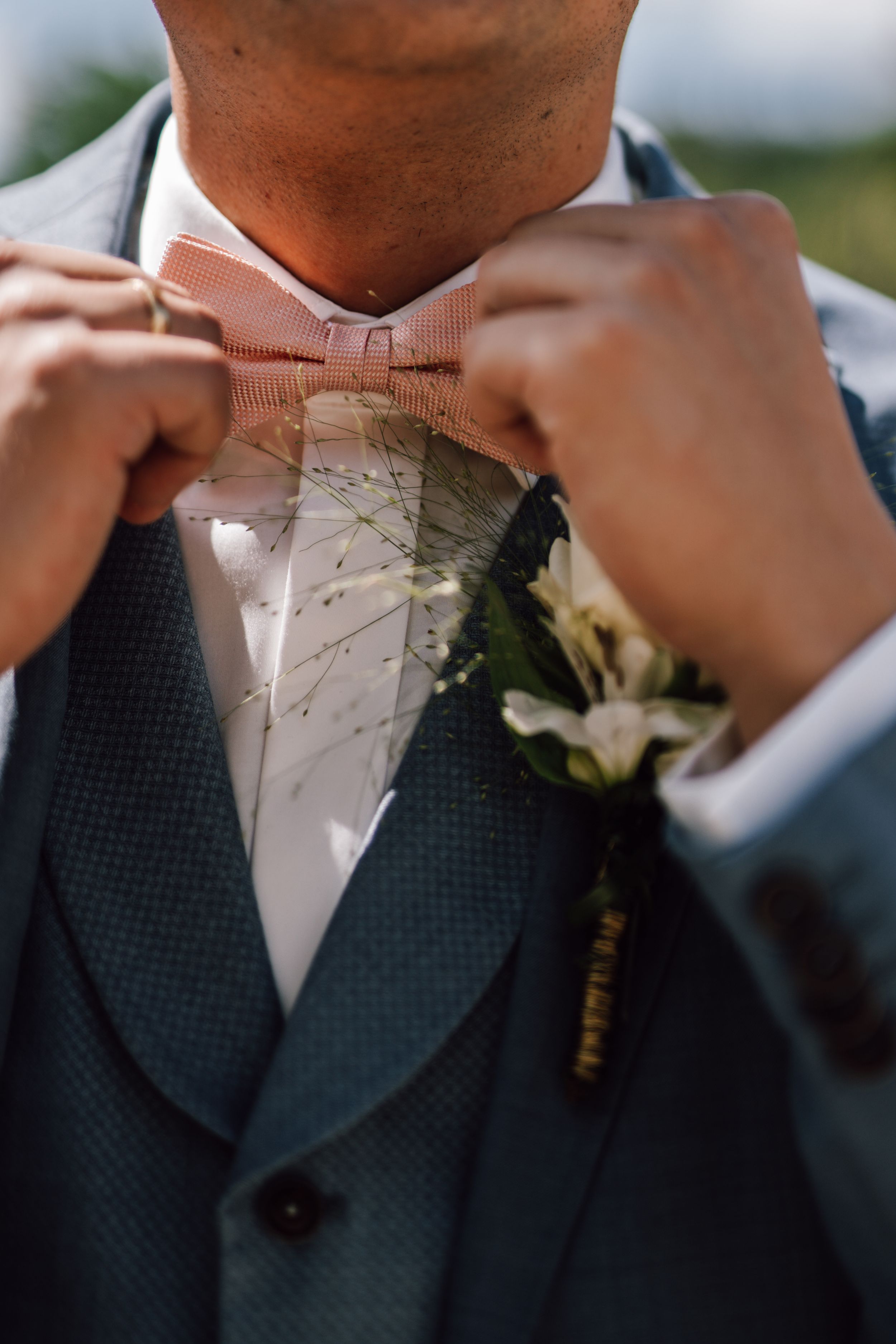Close-up detail of adjusting a white bow tie and boutonniere at a formal wedding.