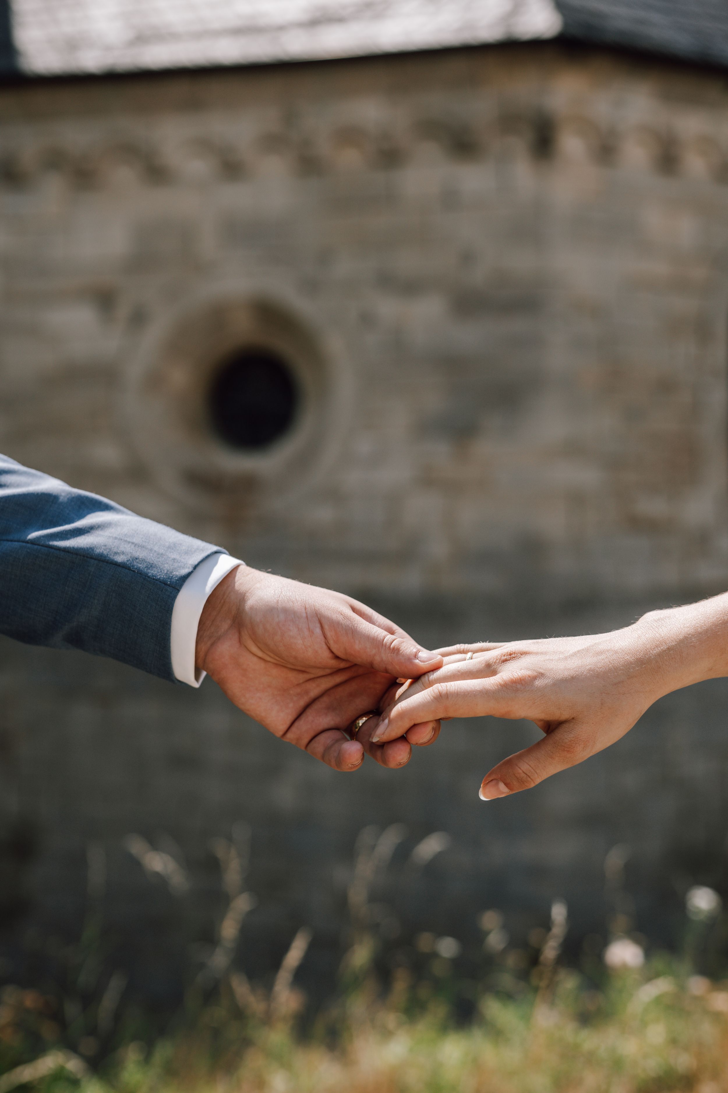 Two hands reaching towards each other against a stone wall background.