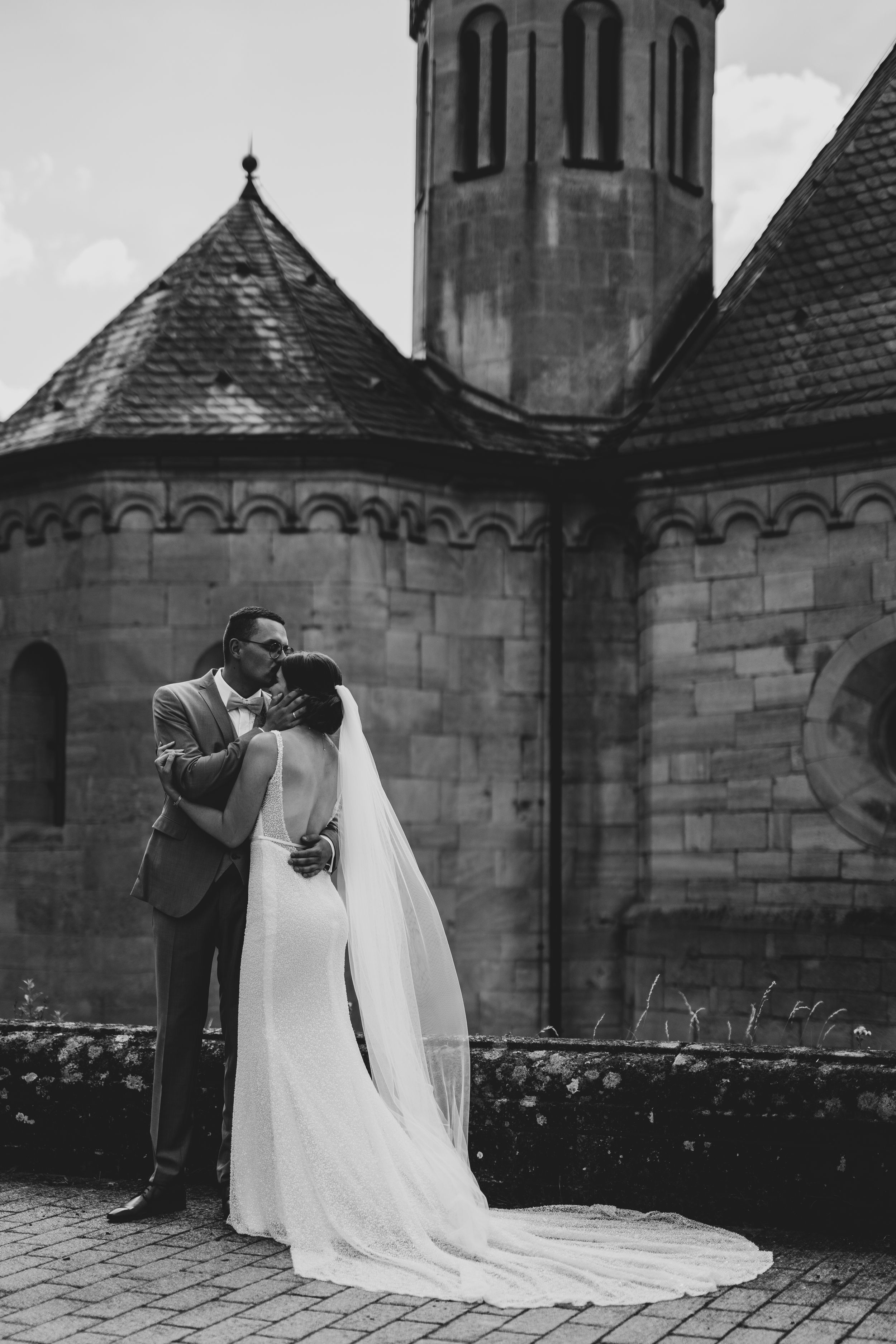 Wedding couple embracing in front of historic stone church architecture.
