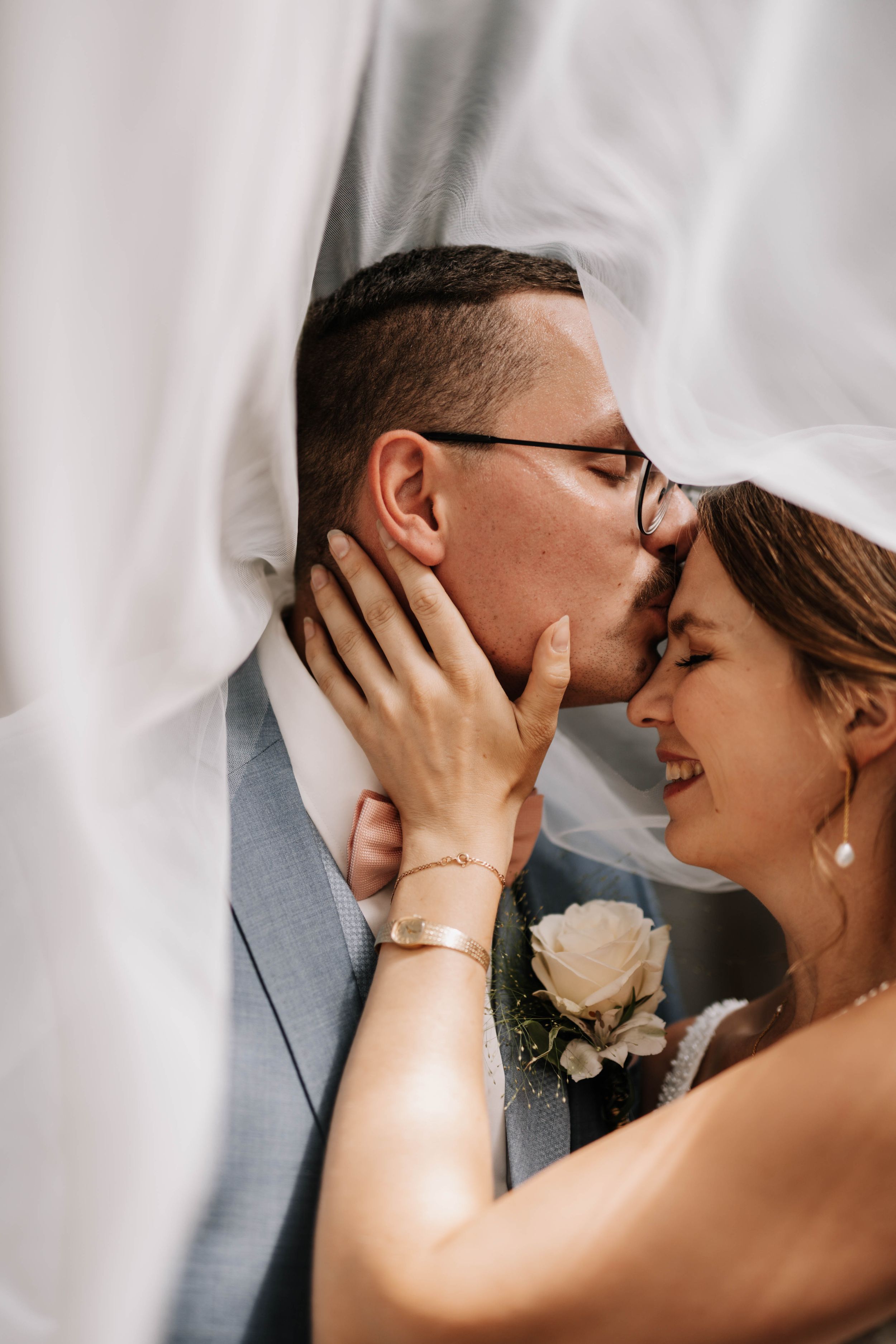 Intimate wedding portrait with flowing white veil in soft lighting.