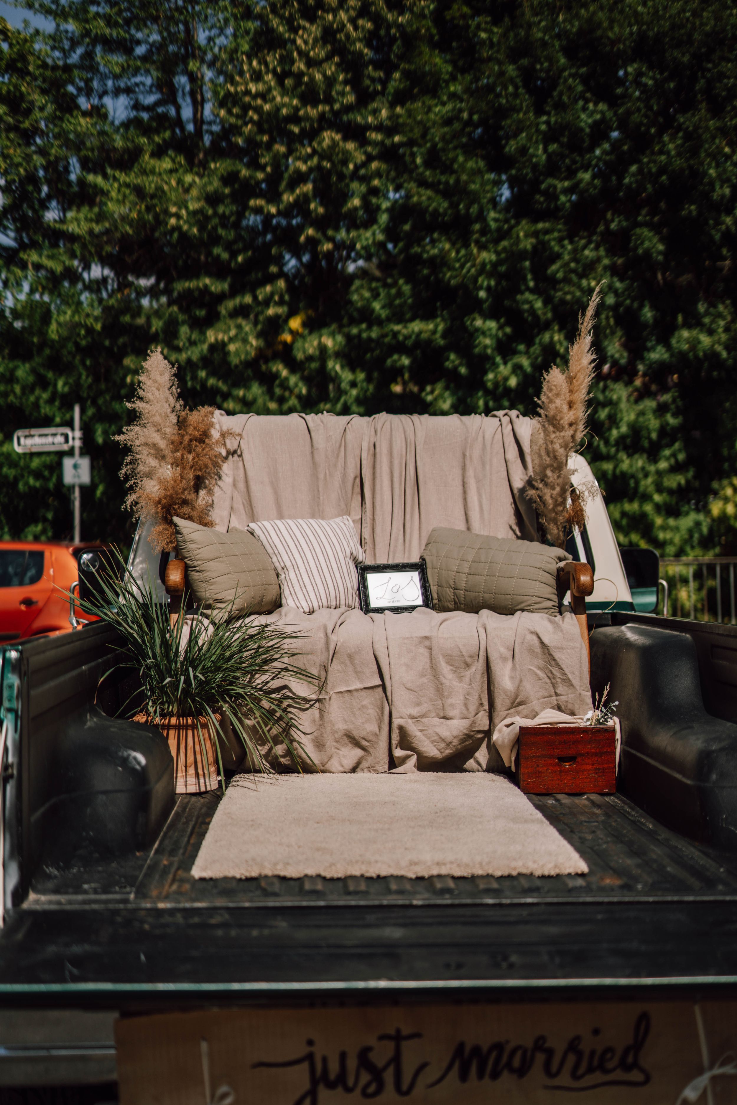 Rustic truck bed decorated with beige fabric, pillows and pampas grass for wedding photos.
