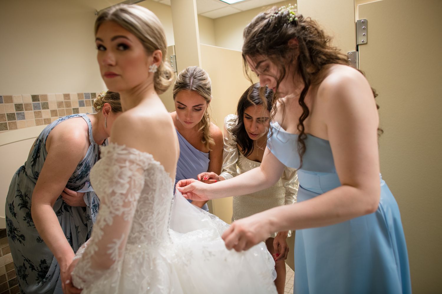 Wedding party getting ready in a warm-toned room with bridesmaids in blue dresses helping with preparations.