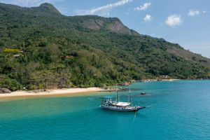 Sailboat anchored near tropical beach with lush mountain backdrop.