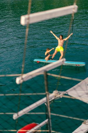 Person in yellow shorts standing on a paddleboard with arms raised triumphantly in turquoise waters.