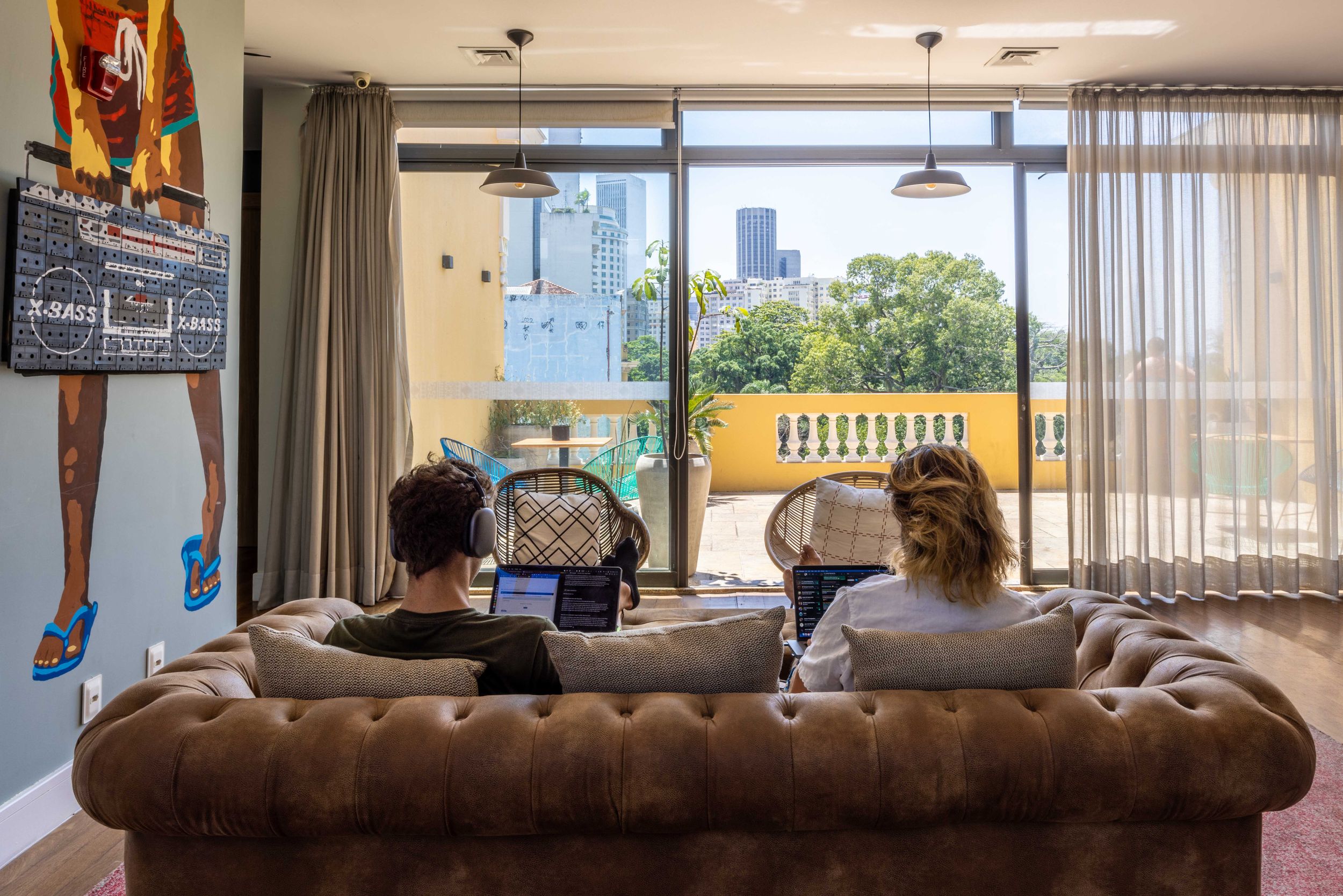 People relaxing on brown leather sofa with city skyline view through large windows.