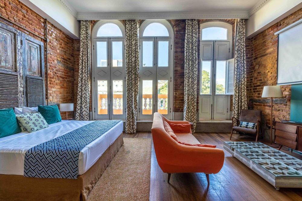 Modern hostel room with exposed brick walls, arched windows, and stylish furniture.