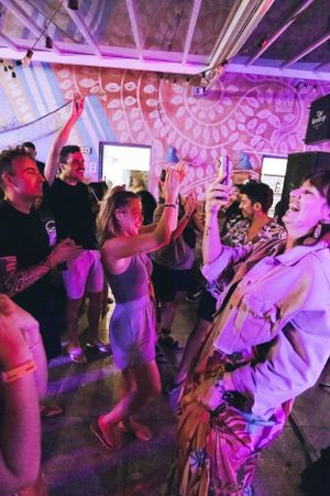 People dancing and celebrating at a nightclub under purple lighting with decorative patterns on the ceiling.
