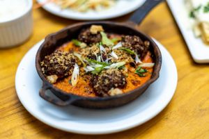 Gourmet dish served in cast iron skillet with creamy sauce and garnishes on white plate.