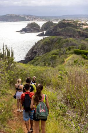 Hikers on coastal trail overlooking dramatic ocean cliffs and turquoise waters.