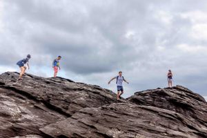 Four people hiking along a rocky ridge against cloudy skies.
