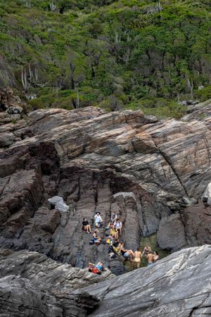 Group of adventurers resting on dramatic coastal rock formations surrounded by green vegetation.
