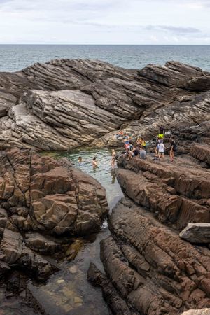 People exploring rocky tide pools near ocean with layered stone formations in foreground.