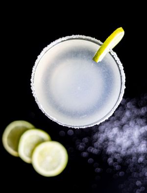 Margarita cocktail with salt rim and lime garnish on black background.