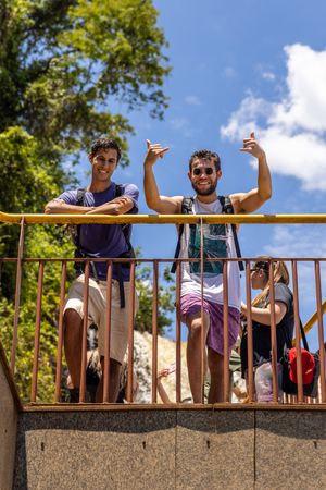 Two people giving thumbs up while standing on a concrete balcony on a sunny day.