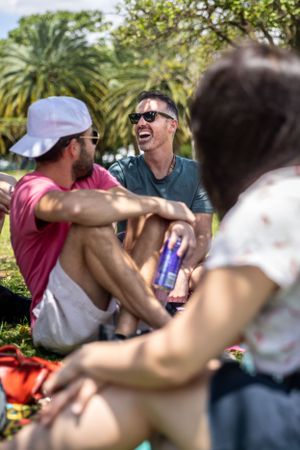 Friends enjoying drinks and conversation during an outdoor picnic in a tropical garden setting.