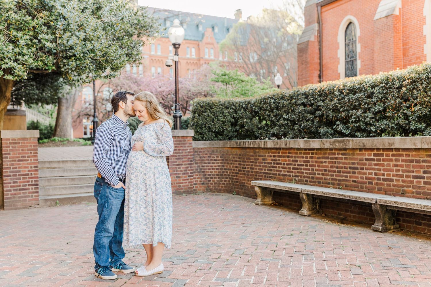A couple strolls along a red brick courtyard with historic buildings in the background.
