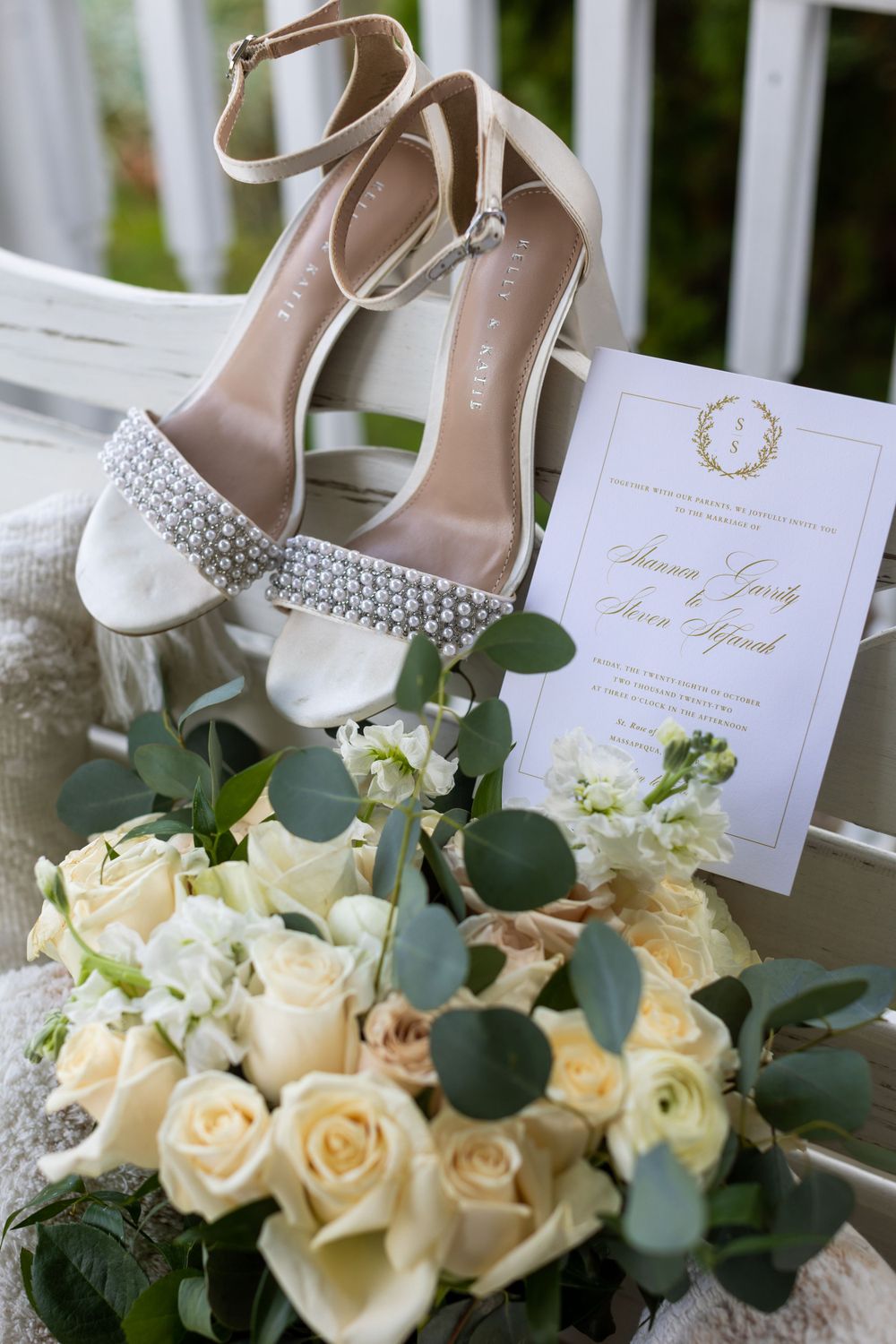 Wedding invitation and sparkly bridal shoes with white rose bouquet and eucalyptus.